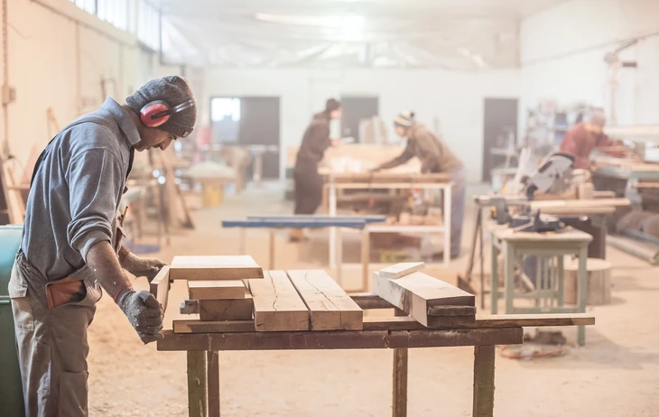 Atelier de menuiserie avec artisan concentré travaillant sur établi, portant protection auditive