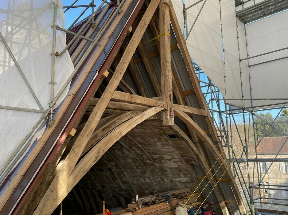 Chantier de restauration d'une charpente ancienne en chêne, sous échafaudage avec bâche de protection
