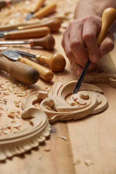 Artisan sculpteur travaillant le bois dans un atelier, utilisant une gouge pour créer des motifs décoratifs sur une pièce ornementale