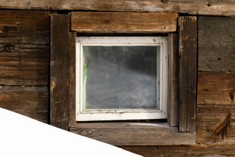 Façade extérieure en bois vieilli d'un chalet traditionnel avec petite fenêtre carrée aux volets ouverts
