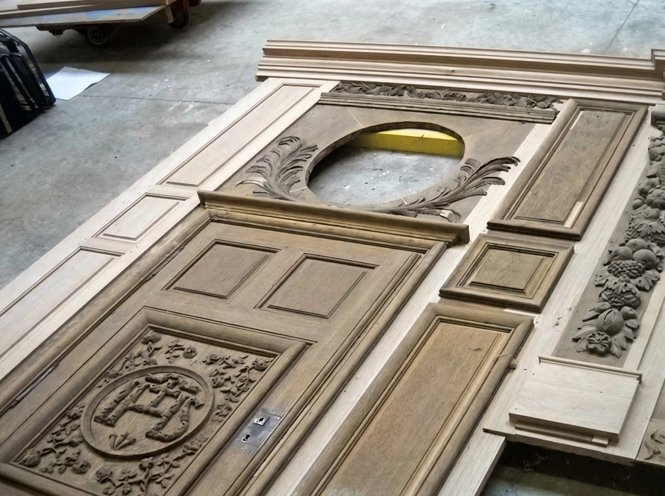 Atelier de menuiserie, vue en plongée sur une boiserie monumentale en chêne brut posée au sol pour assemblage