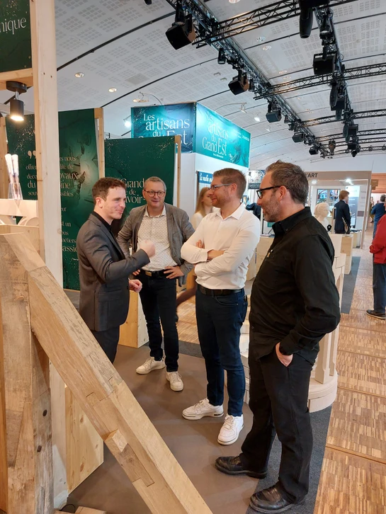 Réunion de travail autour d'une table en bois avec deux personnes consultant des nuanciers de matériaux et plans d'architecture