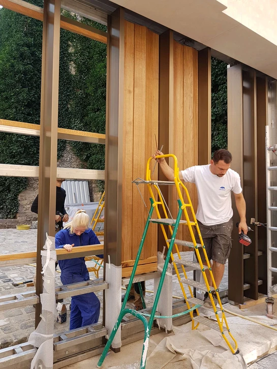Atelier de menuiserie avec deux artisans collaborant sur des plans techniques