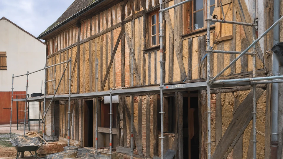 Façade de maison alsacienne à colombages avec murs roses et poutres apparentes en bois foncé